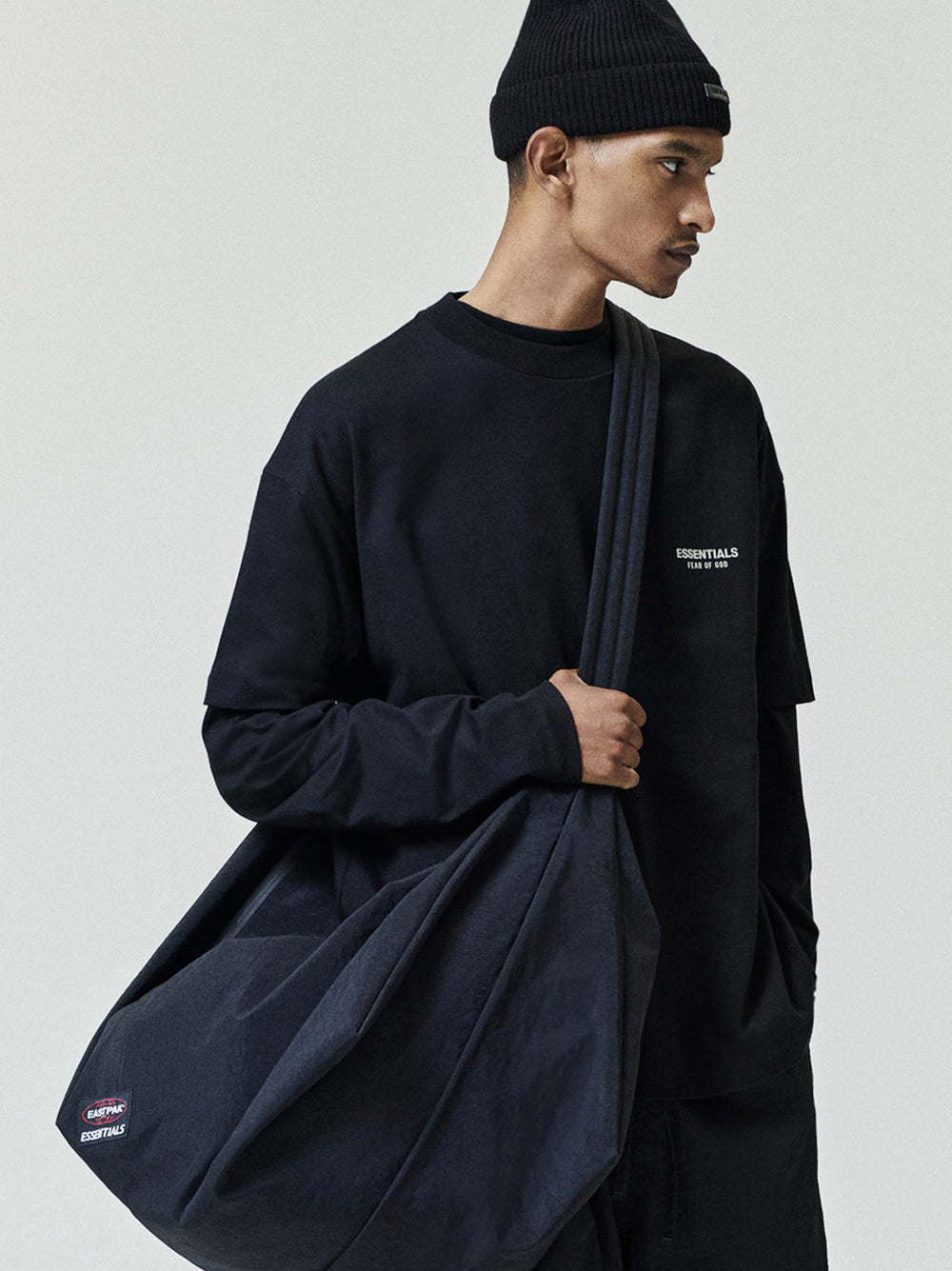 Essentials FW26 Classic Tee in black styled on a model with a black beanie and oversized shoulder bag featuring a subtle chest logo Tops