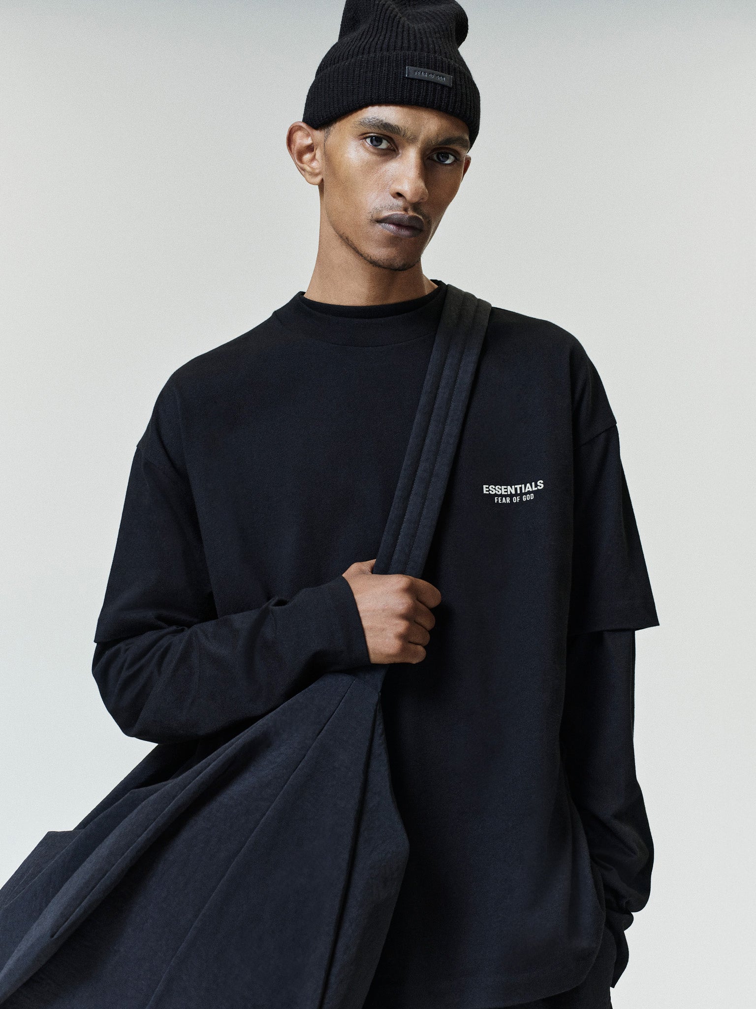 Essentials FW26 Classic Tee in black worn over a long sleeve top with a subtle chest logo and large shoulder bag styled on a model Tops