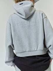 Womens Embossed FW26 Cropped Zip-Up Hoodie in light gray shown from the back with embossed ESSENTIALS Fear of God lettering hood and cropped hem Tops