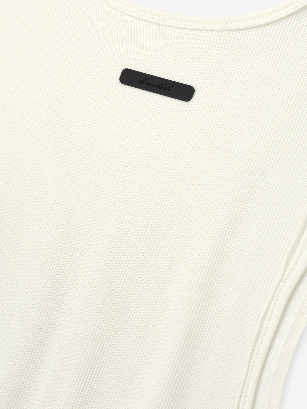 Ribbed Essential Tank in a soft ivory color, made from finely ribbed knit fabric with a close-fitting silhouette and subtle tonal logo detail near the neckline.