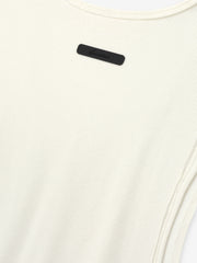 Ribbed Essential Tank in a soft ivory color, made from finely ribbed knit fabric with a close-fitting silhouette and subtle tonal logo detail near the neckline.
