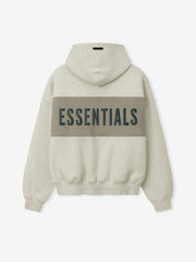 Cropped Relaxed Panelled Hoodie in a light beige tone with a wide muted taupe panel across the back featuring bold dark "ESSENTIALS" lettering, designed with ribbed cuffs and hem for a cozy fit.