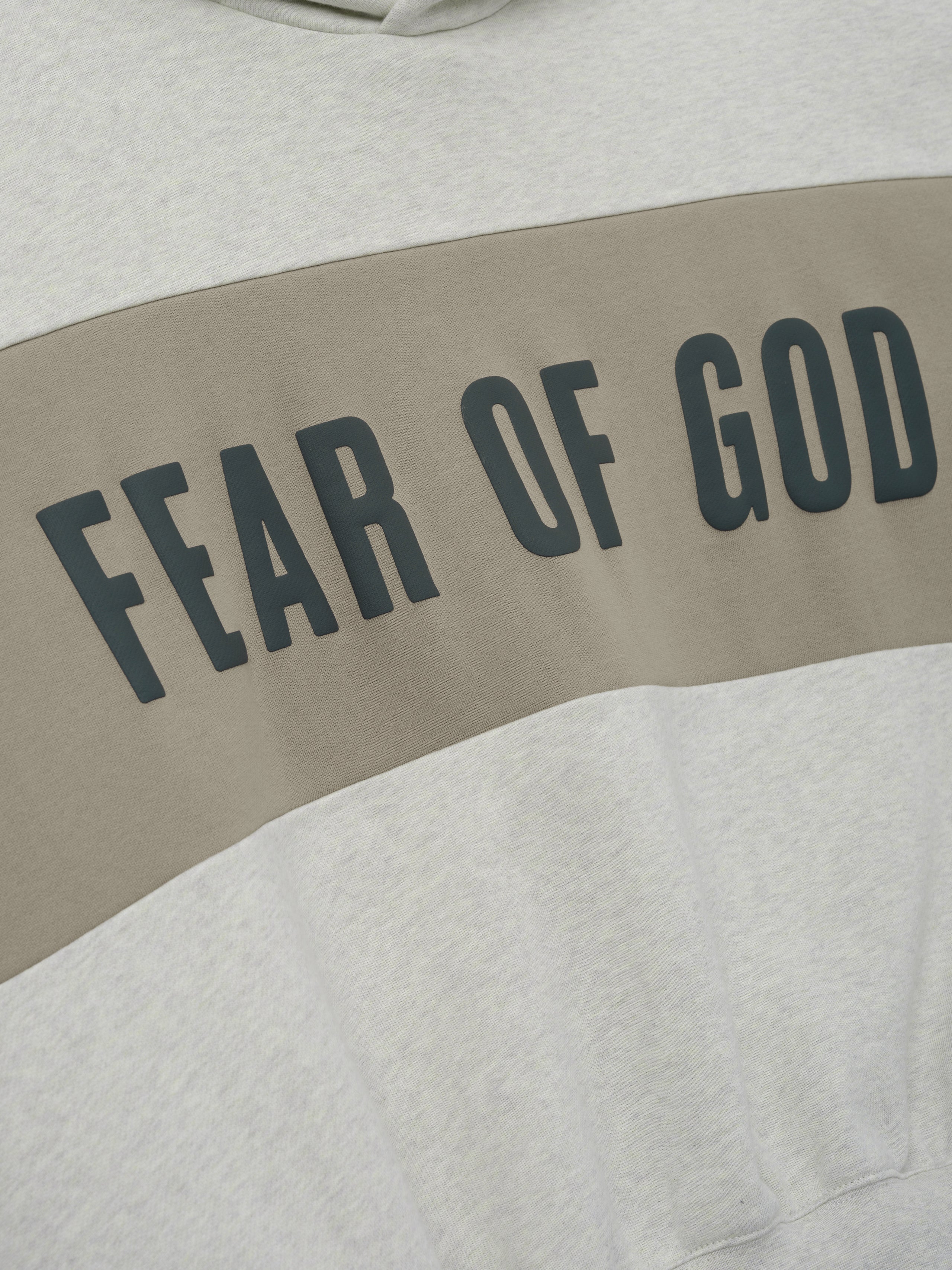 Cropped Relaxed Panelled Hoodie featuring a soft vanilla heather fabric with a wide muted taupe panel across the chest displaying bold black Fear of God lettering for a stylish streetwear look.