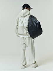 90'S Zip-Up Hoodie in a soft washed vanilla heather shade with an oversized fit, featuring bold white numbers on the back and styled with relaxed matching pants and a large black textured bag.
