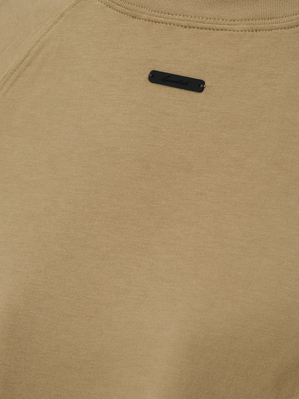 Womens Tri-Blend Shrunken Baseball Tee in a muted dune tone with soft texture, featuring a small black branded patch near the neckline, crafted as a casual top.