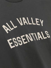 Merch Long Sleeve Tee in dark grey featuring cracked cream "ALL VALLEY ESSENTIALS" text printed on soft fabric for a comfortable casual top.