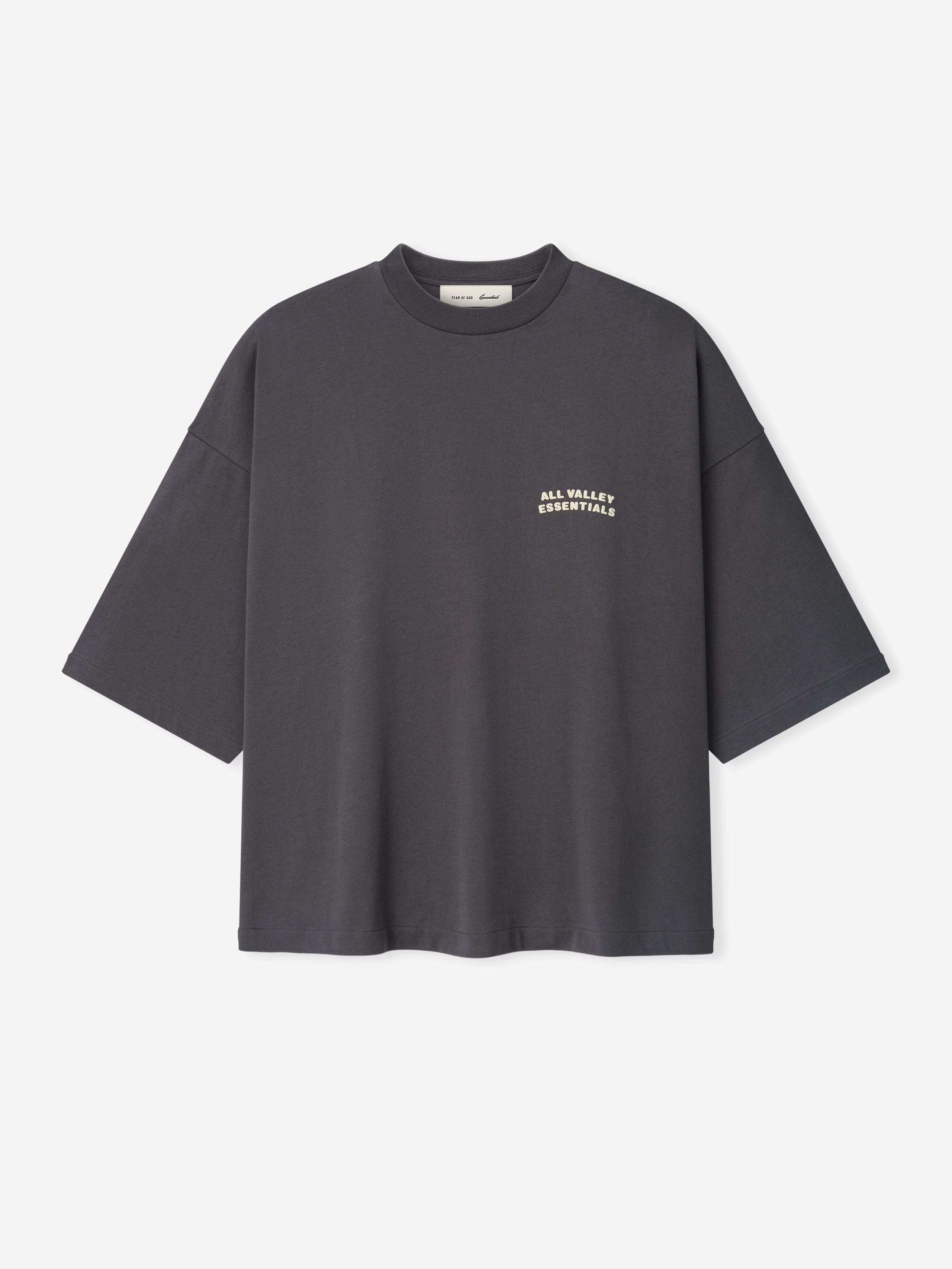 Merch Tee in dark iron grey featuring a relaxed oversized fit with dropped shoulders and small cream text "ALL VALLEY ESSENTIALS" on the chest for a minimalist casual top.