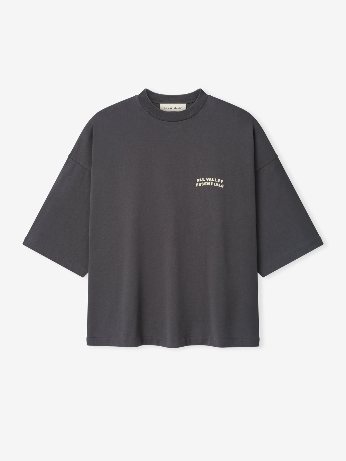 Merch Tee in dark iron grey featuring a relaxed oversized fit with dropped shoulders and small cream text "ALL VALLEY ESSENTIALS" on the chest for a minimalist casual top.