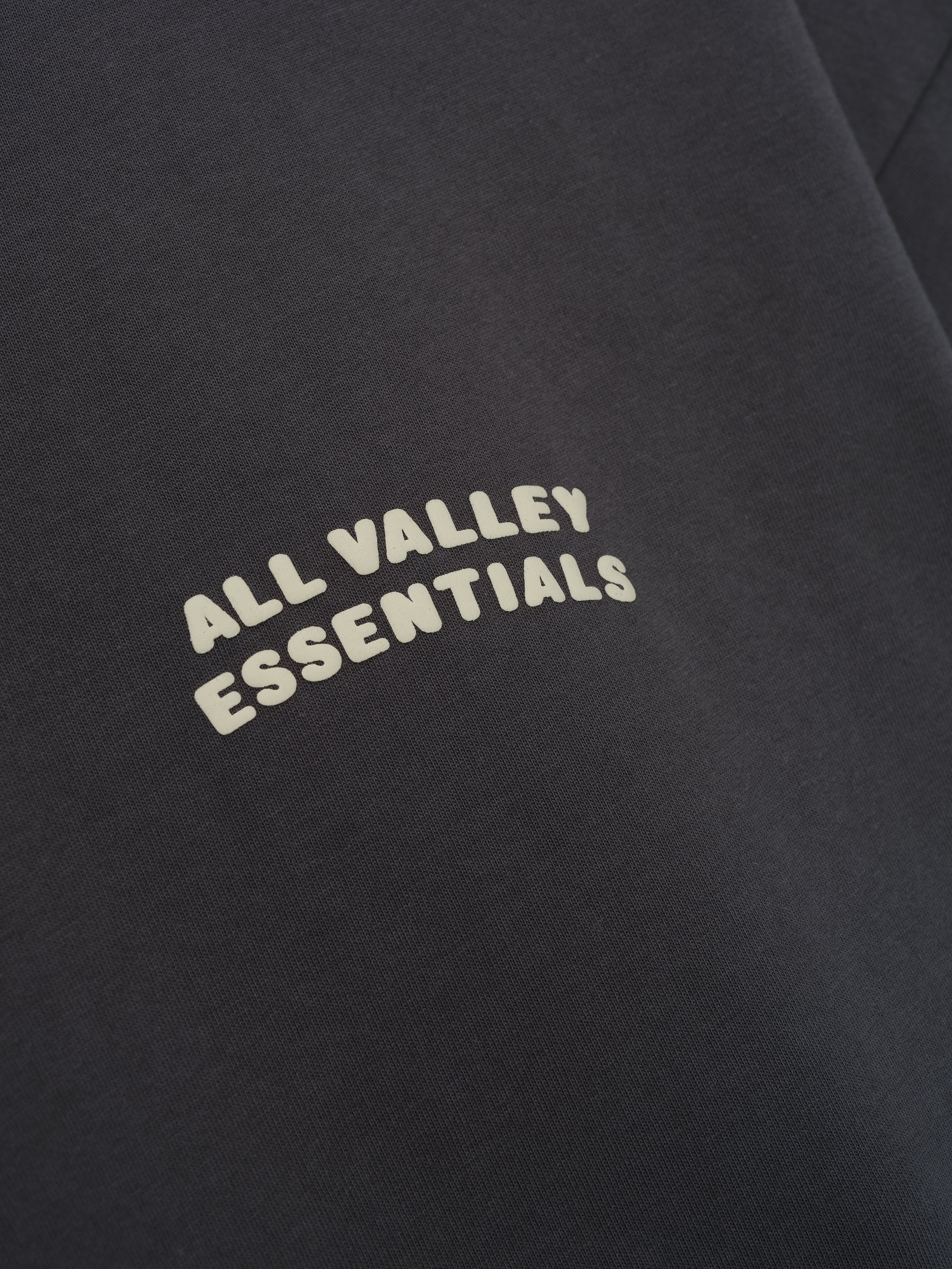Merch Tee in deep iron grey featuring soft fabric with a minimalist curved cream "ALL VALLEY ESSENTIALS" text printed on the chest for a clean, casual top.