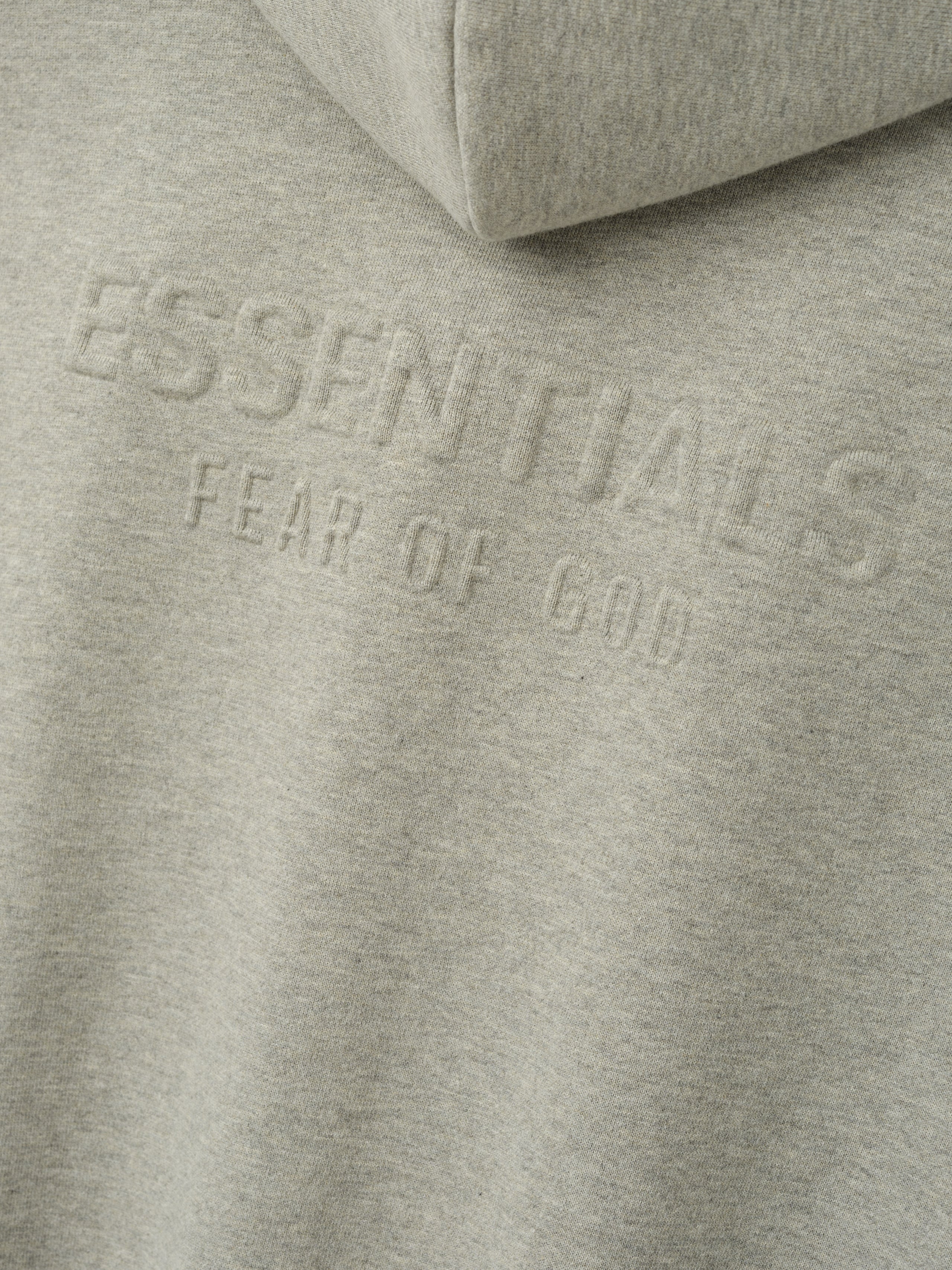 Womens Embossed FW26 Cropped Zip-Up Hoodie in light gray close-up with tonal ESSENTIALS Fear of God embossed lettering and soft fleece texture Tops