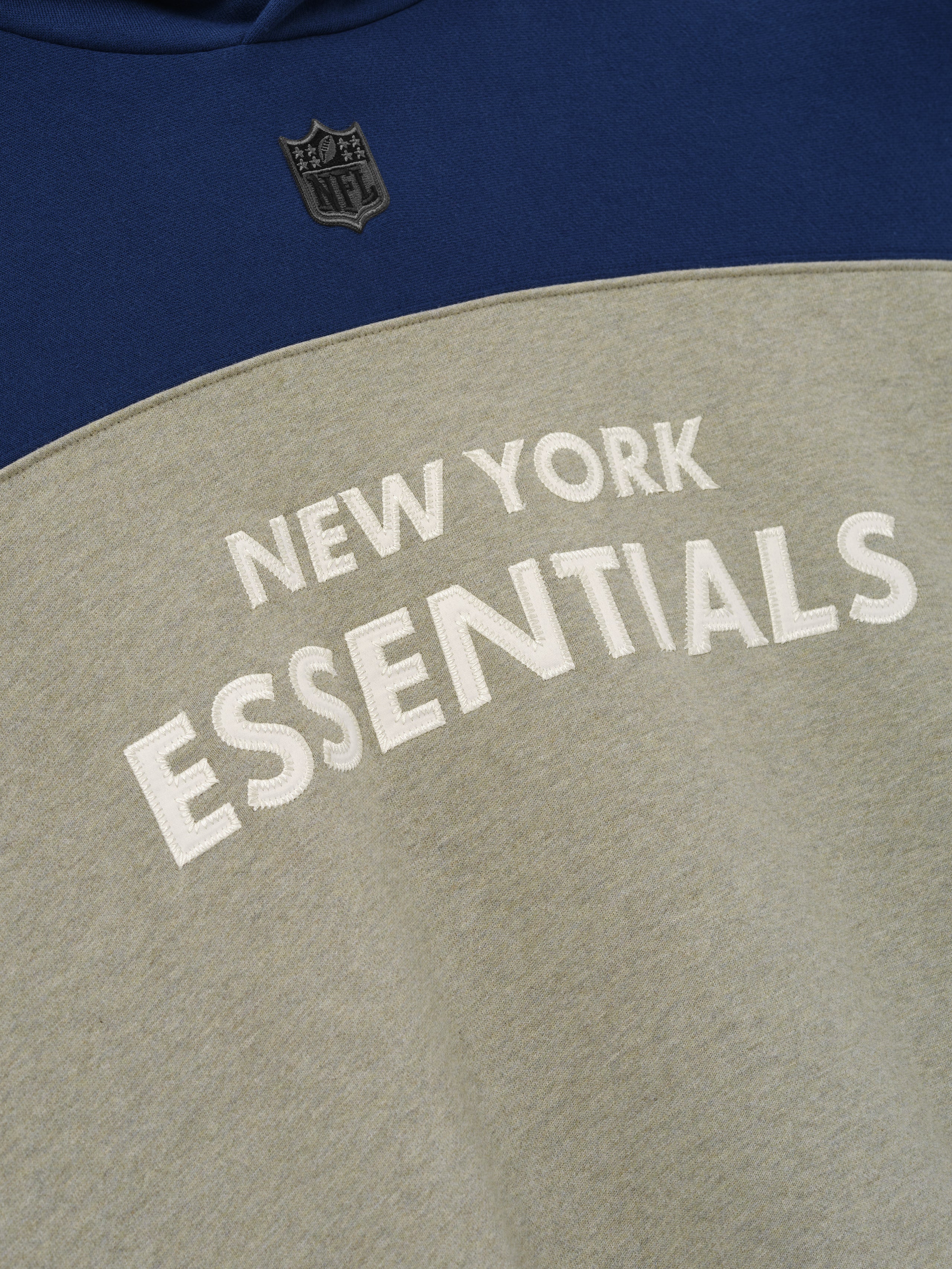 Giants 90s Relaxed Hoodie close up showing white New York Essentials lettering and NFL shield on navy blue and gray fleece as a Tops product detail
