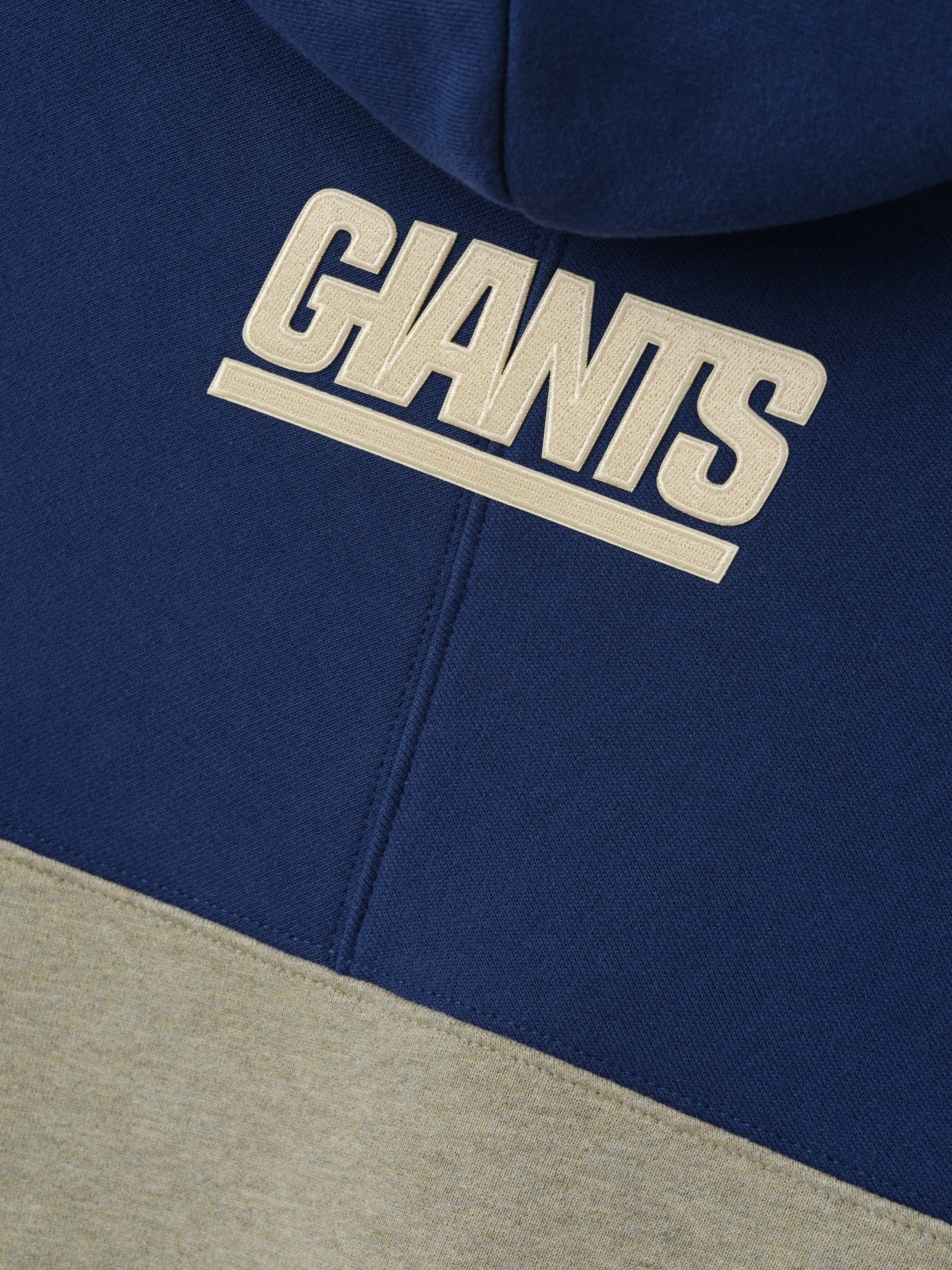 Giants 90s Relaxed Hoodie close up showing raised cream Giants lettering on navy fleece above a gray color block as a Tops product detail